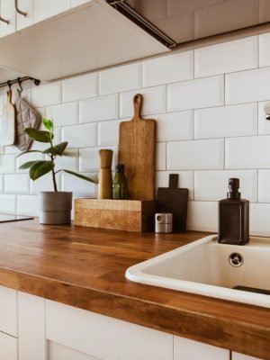 Kitchen brass utensils, chef accessories. Hanging kitchen with white tiles wall and wood tabletop.Green plant on kitchen background side view