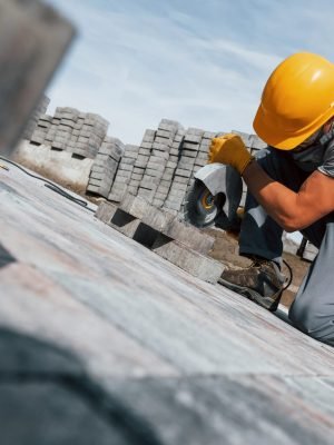 Slicing by circular saw. Male worker in yellow colored uniform have job with pavement.